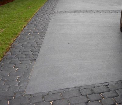 Weathered and worn brick paver stamped concrete edging, with plain gray textured driveway.
