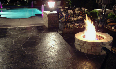 Dark brown stamped patio with built in fire pit, next to concrete pool deck.